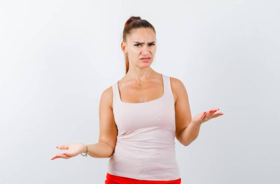Woman in a beige top and red pants, showing a helpless gesture and looking confused.