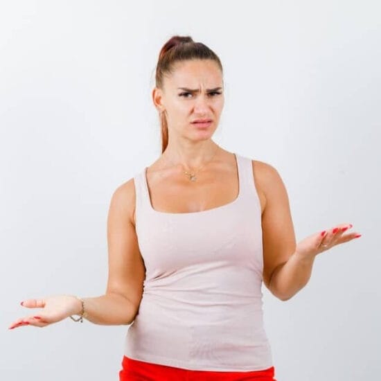Woman in a beige top and red pants, showing a helpless gesture and looking confused.