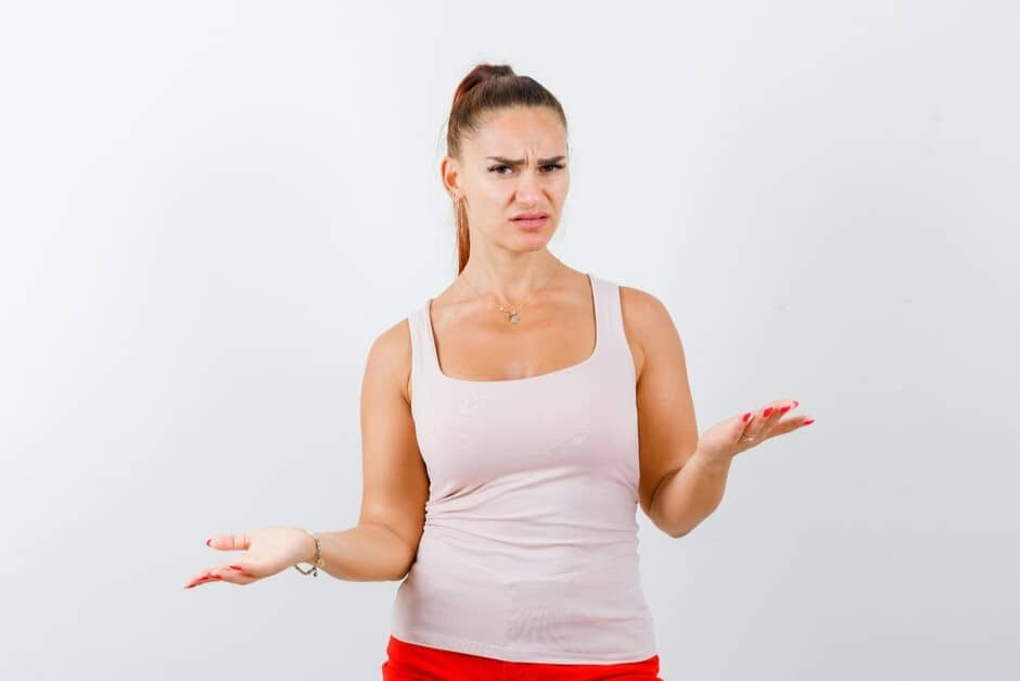 Woman in a beige top and red pants, showing a helpless gesture and looking confused.