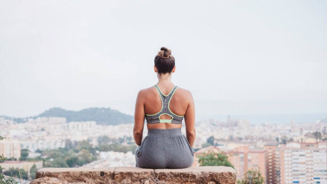 Back view of woman sitting on rock in front of city