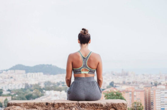 Back view of woman sitting on rock in front of city