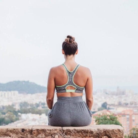 Back view of woman sitting on rock in front of city